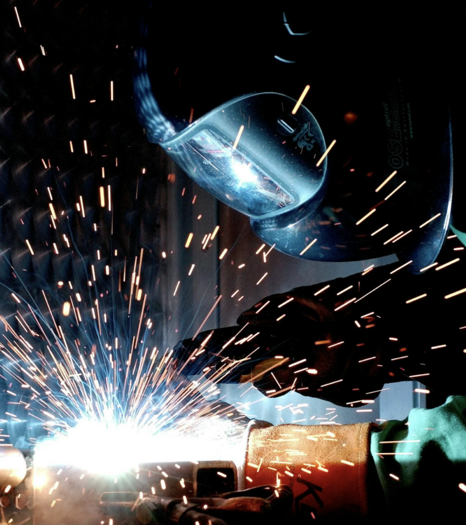 Welder with dark helmet and gloves welding with sparks flying